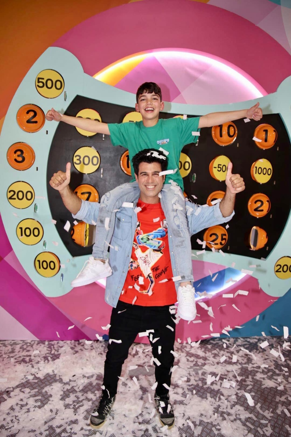 יהלי מנצח ששטוס מונף על הכתפיים של מנחה ערוץ הילדים טל מוסרי