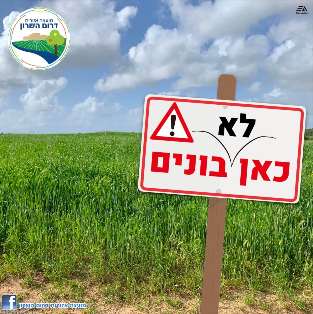מודעה גרפית שלט עם הכיתוב כאן לא בונים על רקע שדה חקלאי בדרום השרון